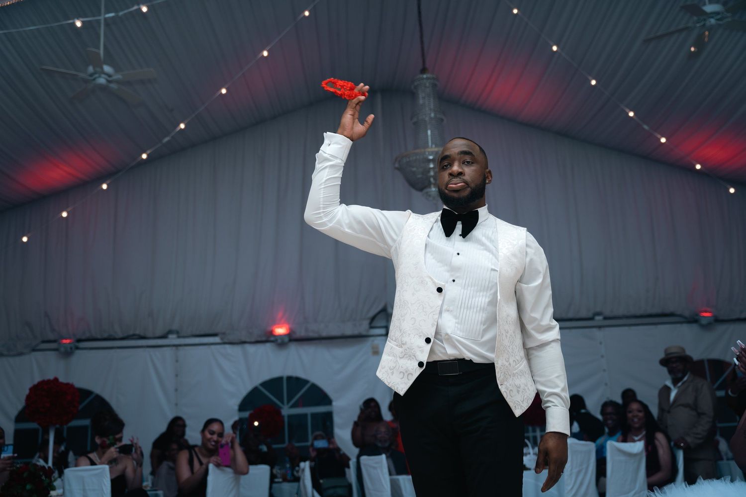Person in white dinner jacket raising a celebratory toast at an evening reception.