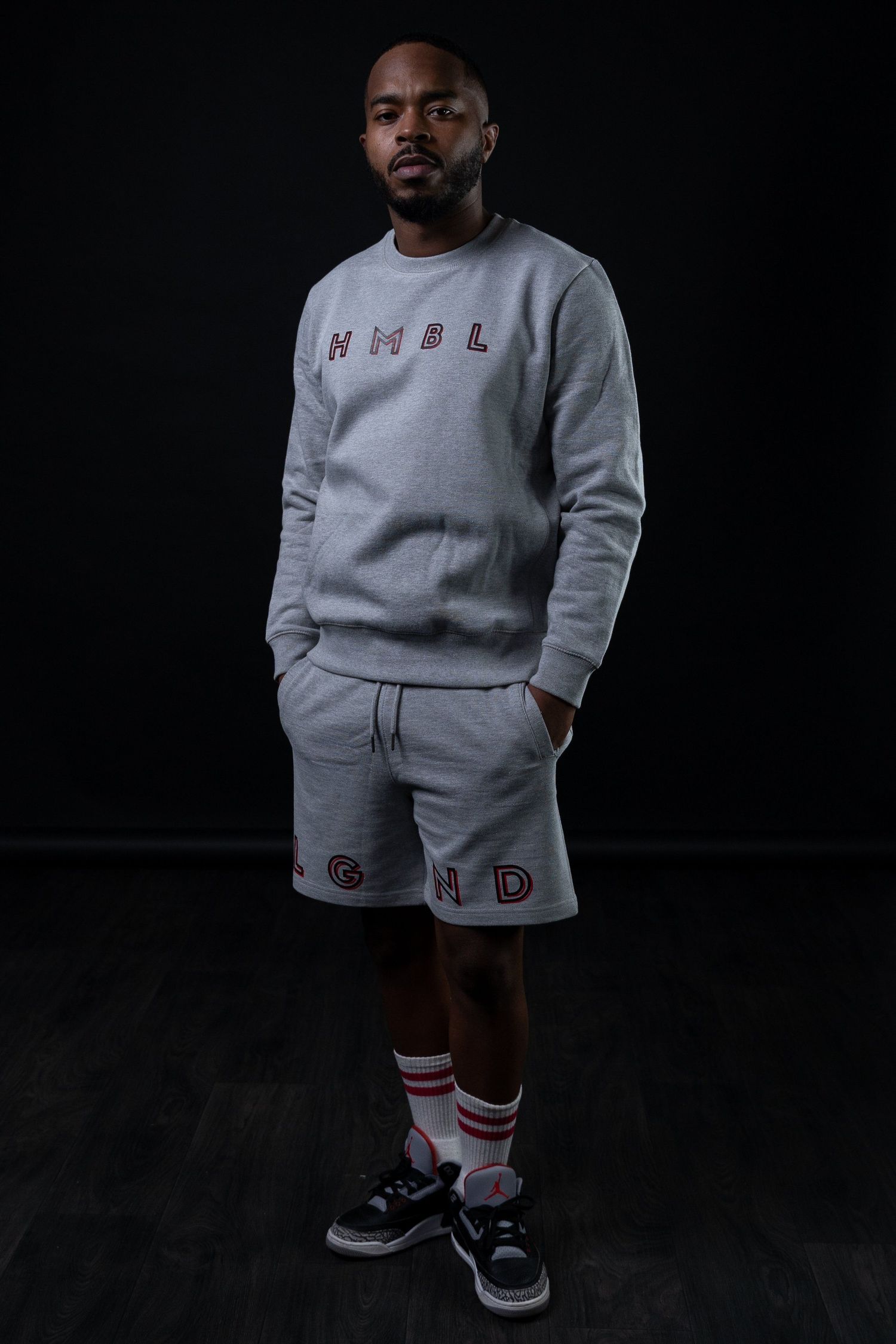 Person wearing grey matching sweatsuit and Nike sneakers poses against dark background.