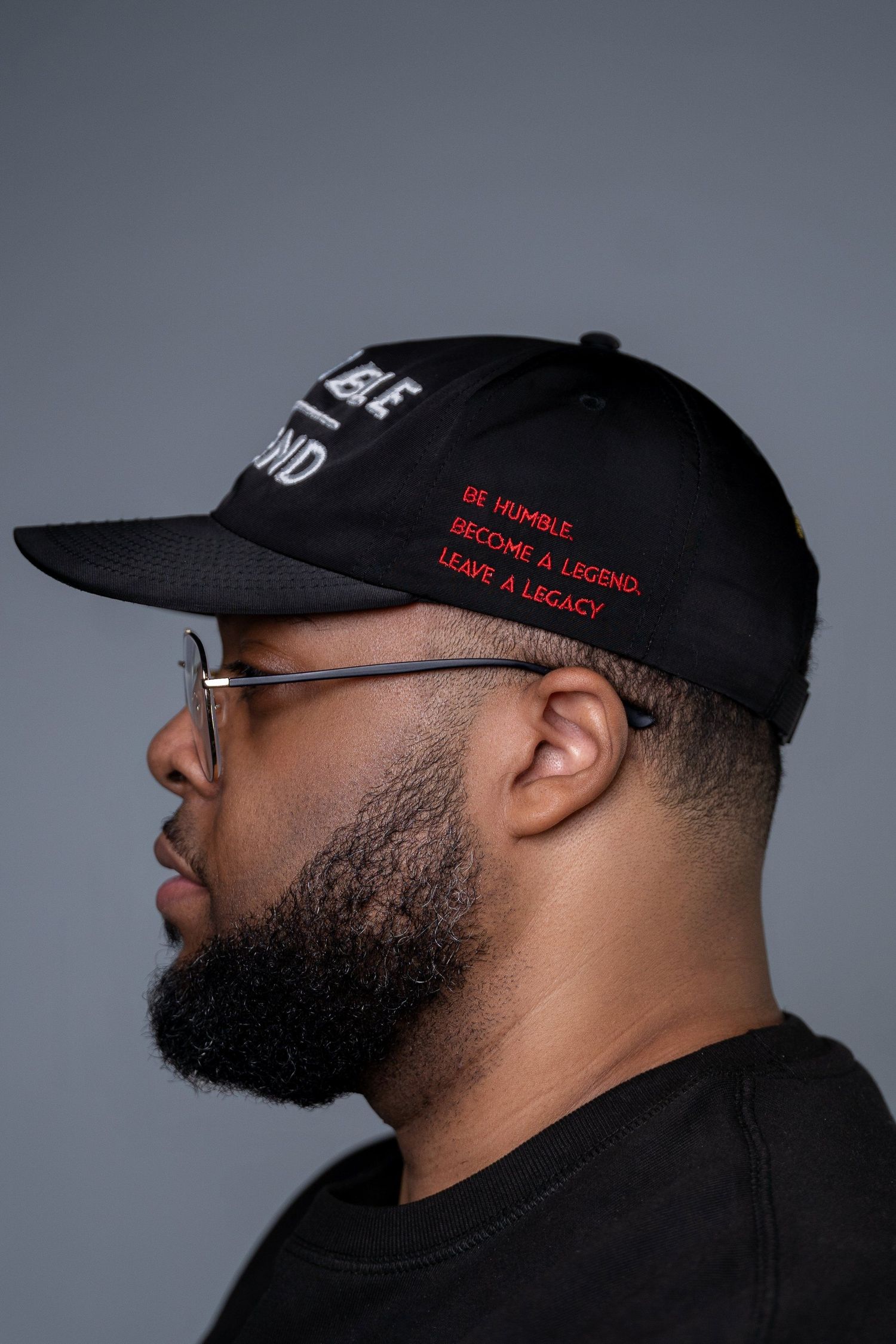 Side profile of person wearing black baseball cap with red text against grey background.