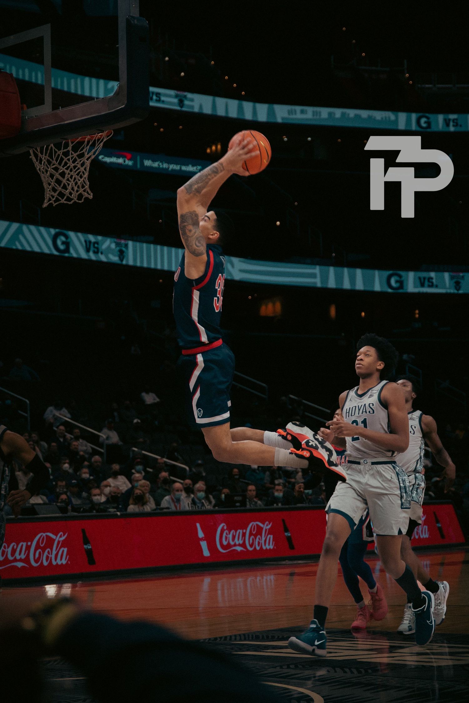 Basketball player soaring for slam dunk during professional game with Coca-Cola advertisement visible.