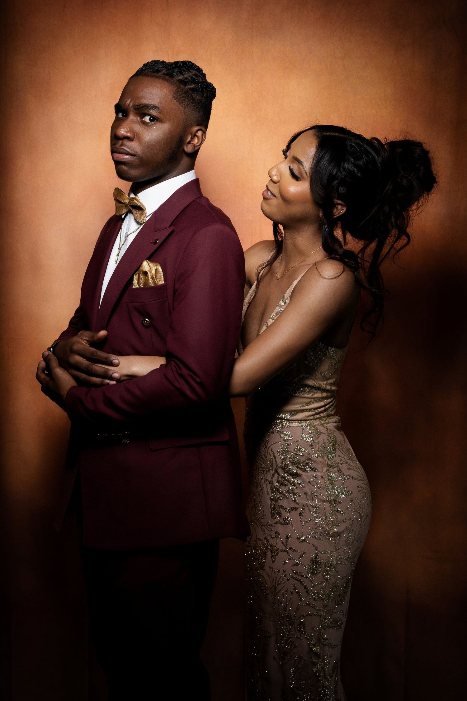 Romantic formal portrait of a couple in burgundy and gold against a warm brown backdrop.