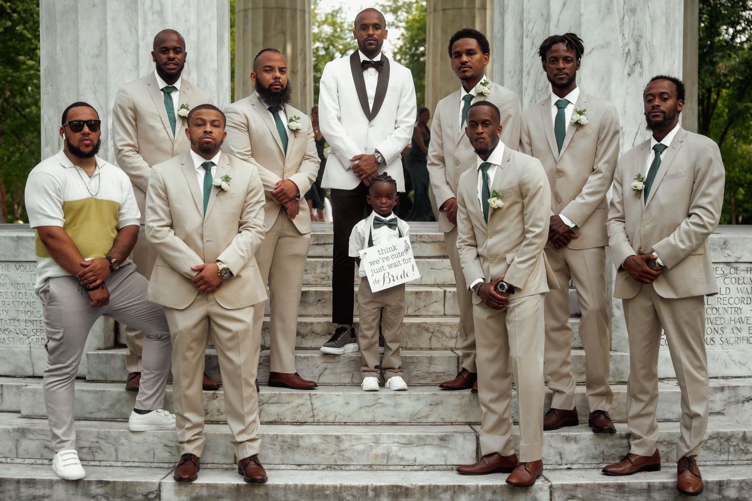 Groomsmen in matching beige suits posing on stone steps for formal wedding photo.
