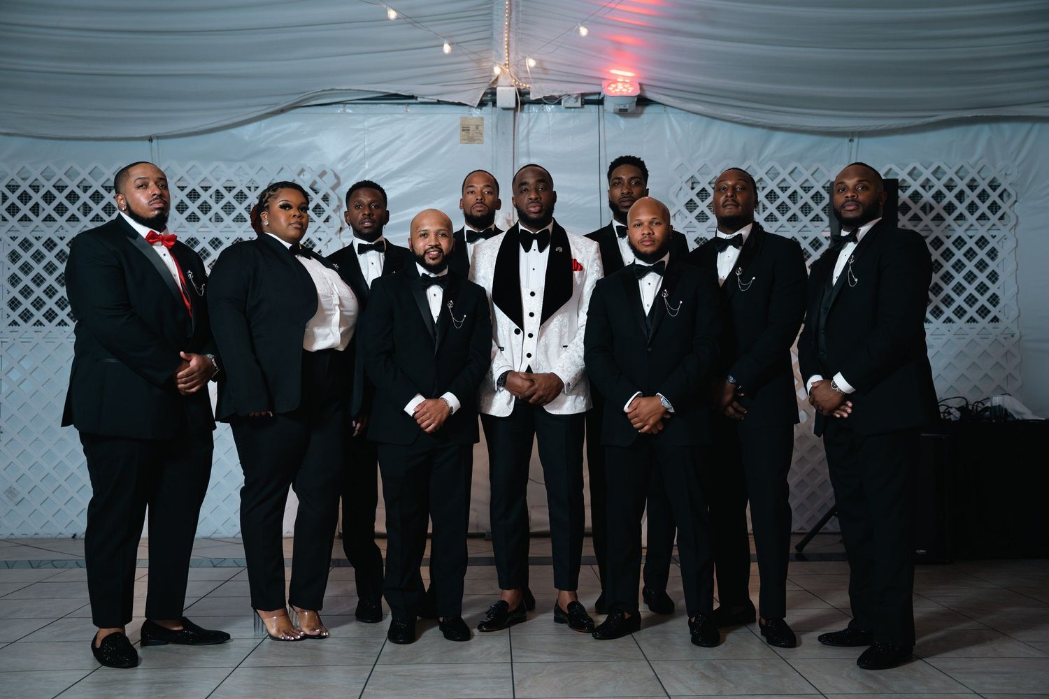 Group photo of wedding party members in formal black tie attire at reception venue.