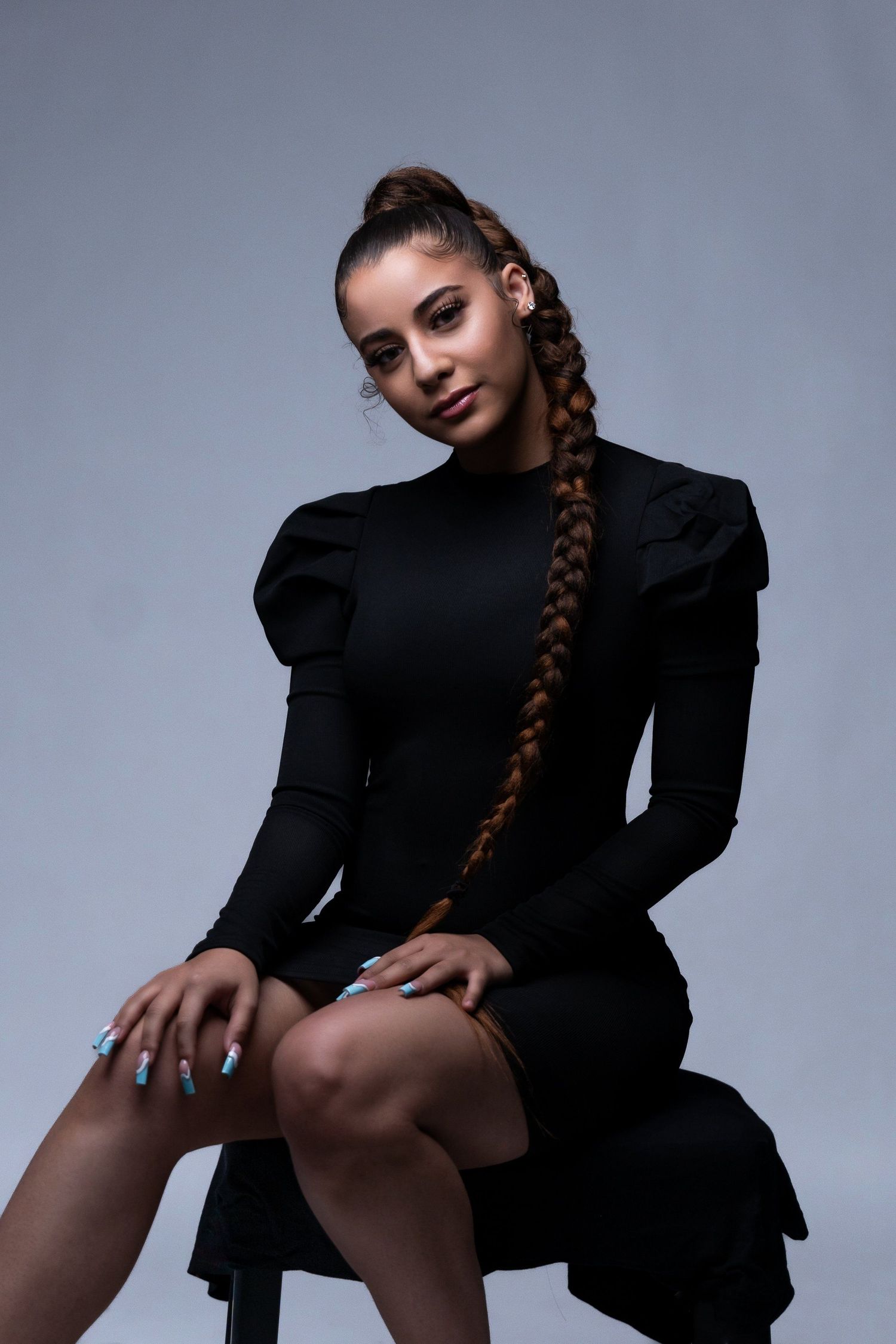 Fashion portrait featuring long braided hair and black dress against grey background.
