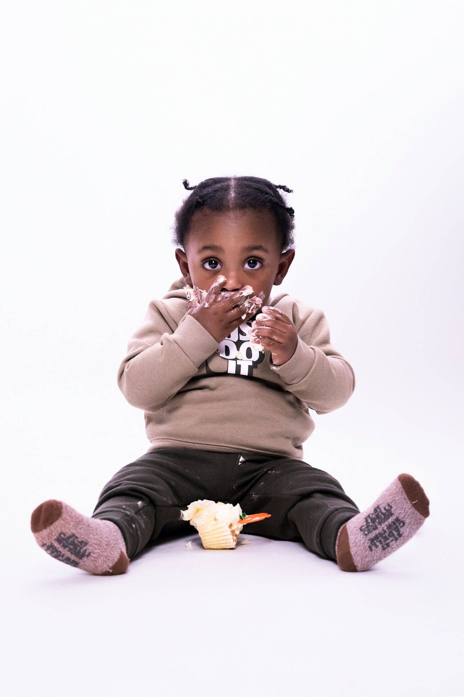 Small child in beige sweater sitting on floor with socks, holding a snack and giggling.