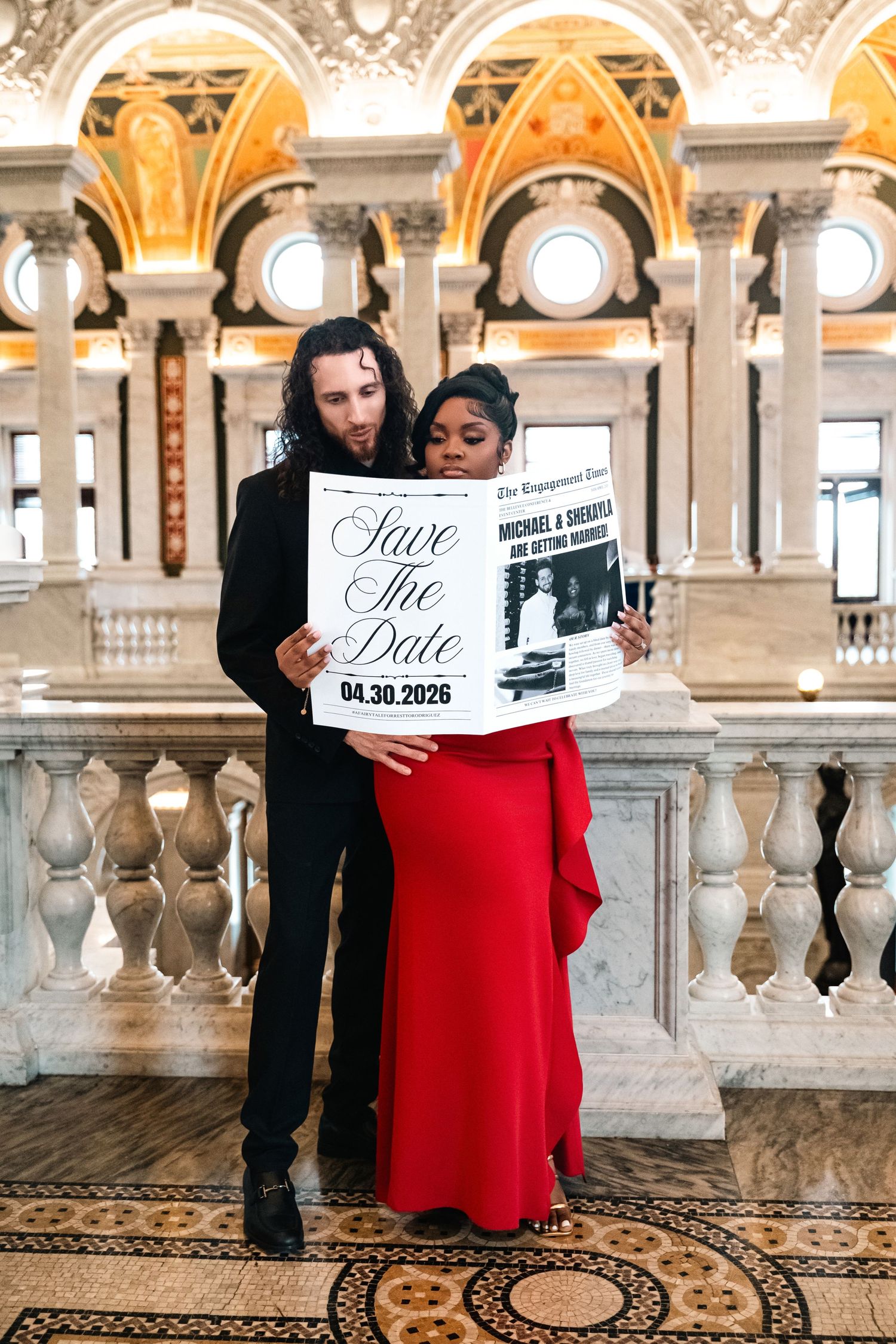 Engaged couple holding a save the date announcement in a luxurious ornate hallway with golden archways and marble columns.