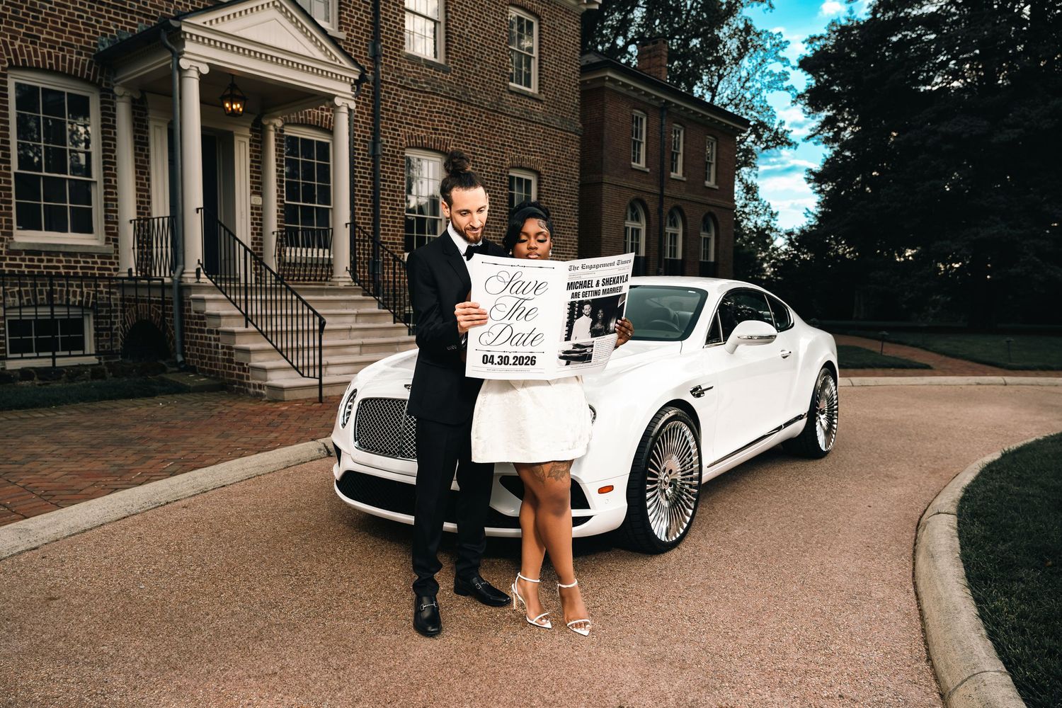 A couple stands in front of a luxury white car on a circular driveway of a brick building with columns.