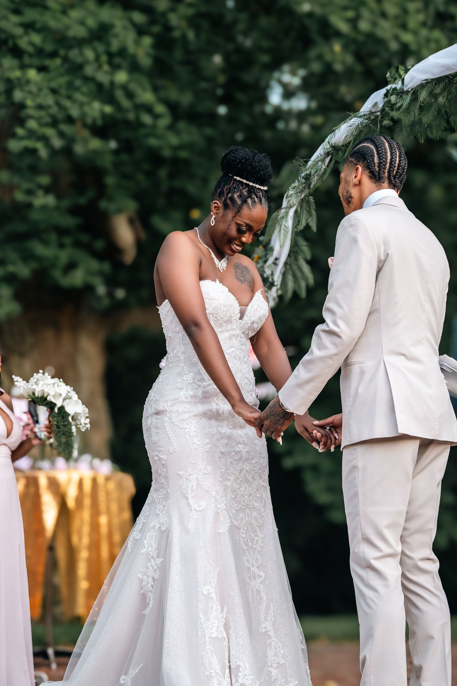 Couple holding hands during outdoor wedding ceremony under floral arch.