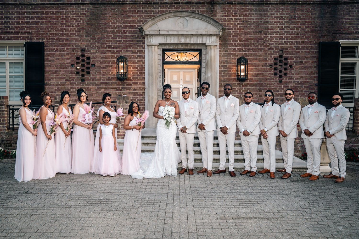 Wedding party in pink and white attire poses in front of brick building.
