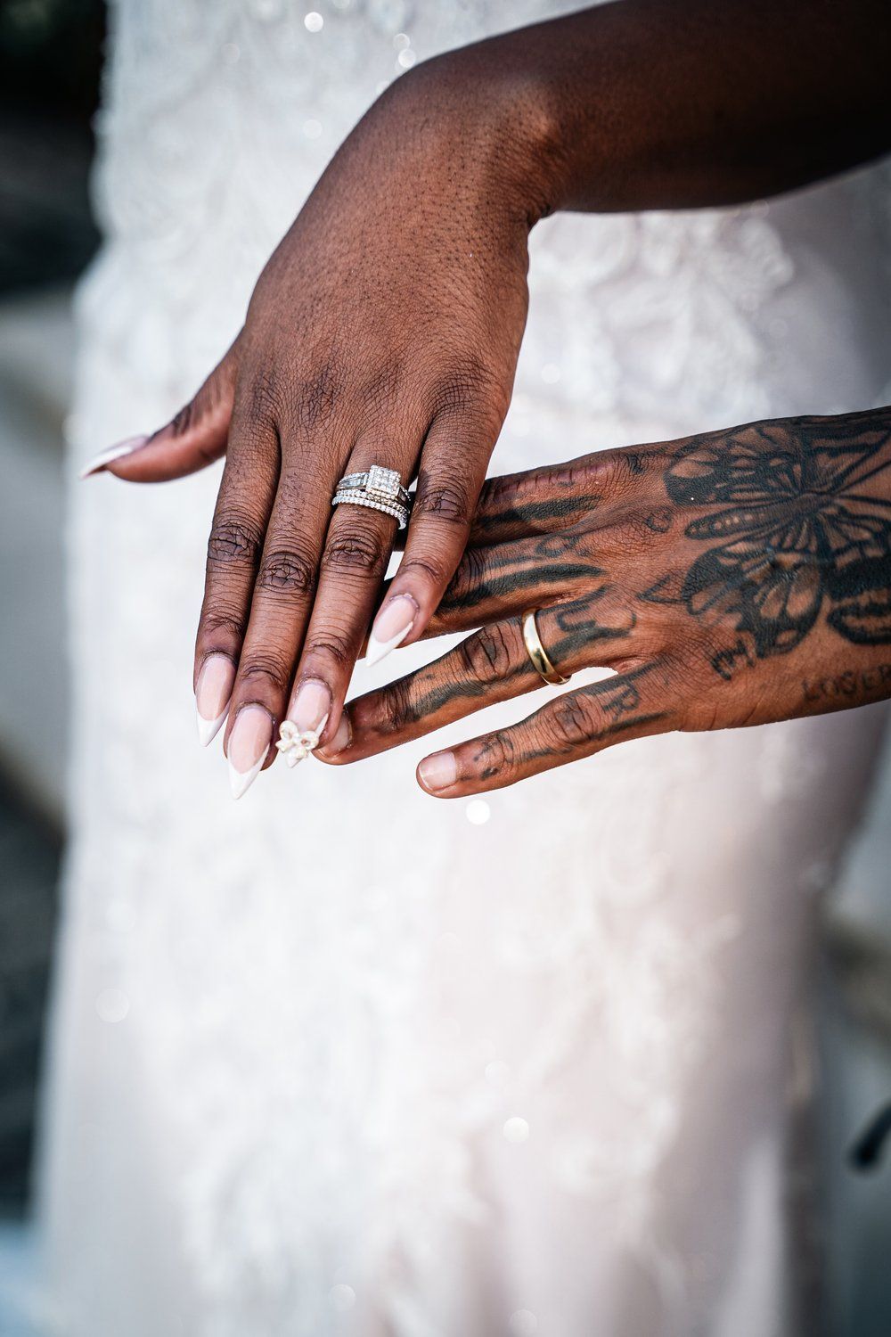 Close-up of hands showing wedding rings and intricate butterfly tattoo artwork.