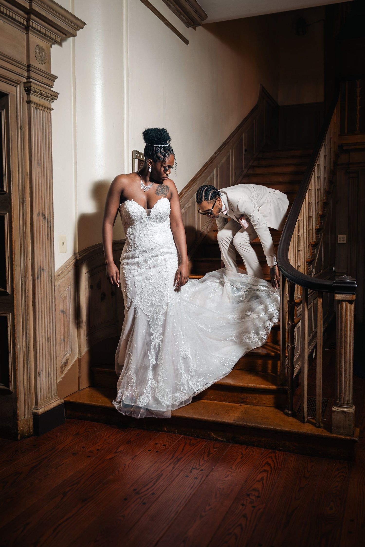 Bride on staircase with elegant white lace dress being adjusted.