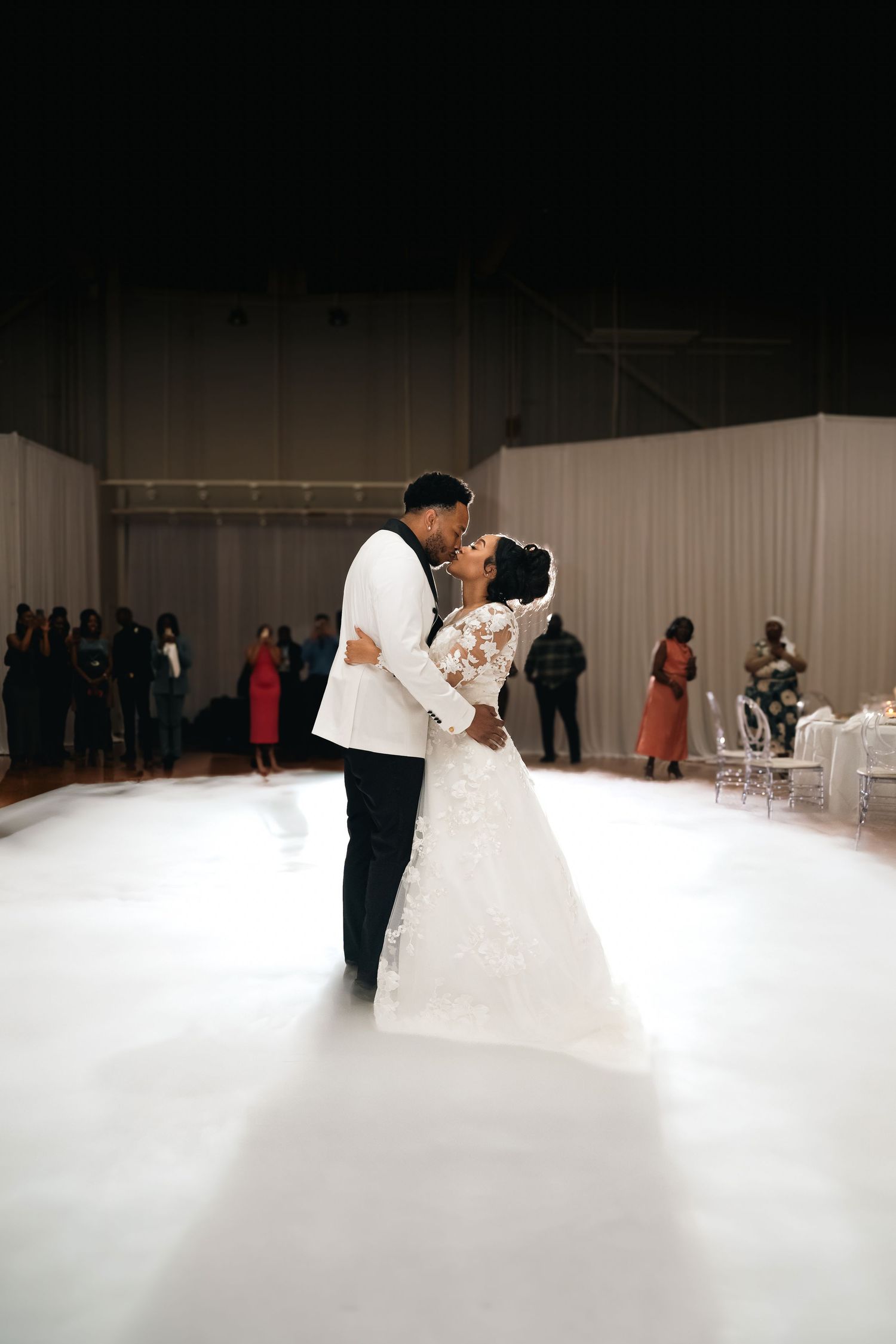 Couple sharing romantic first dance on misty white dancefloor at wedding reception.