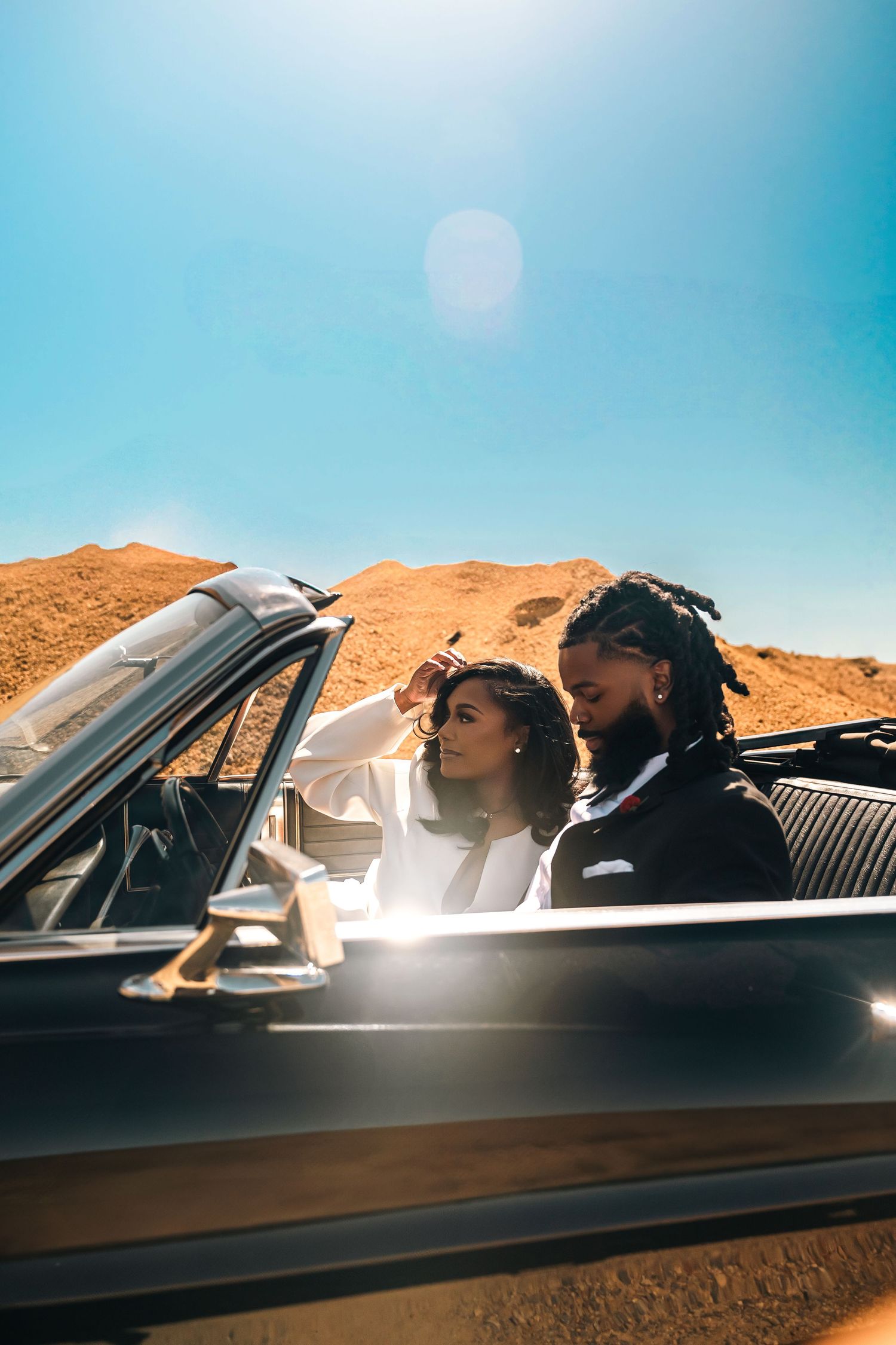 Couple enjoying a sunny drive through desert mountains in a vintage convertible car with dramatic lens flare.
