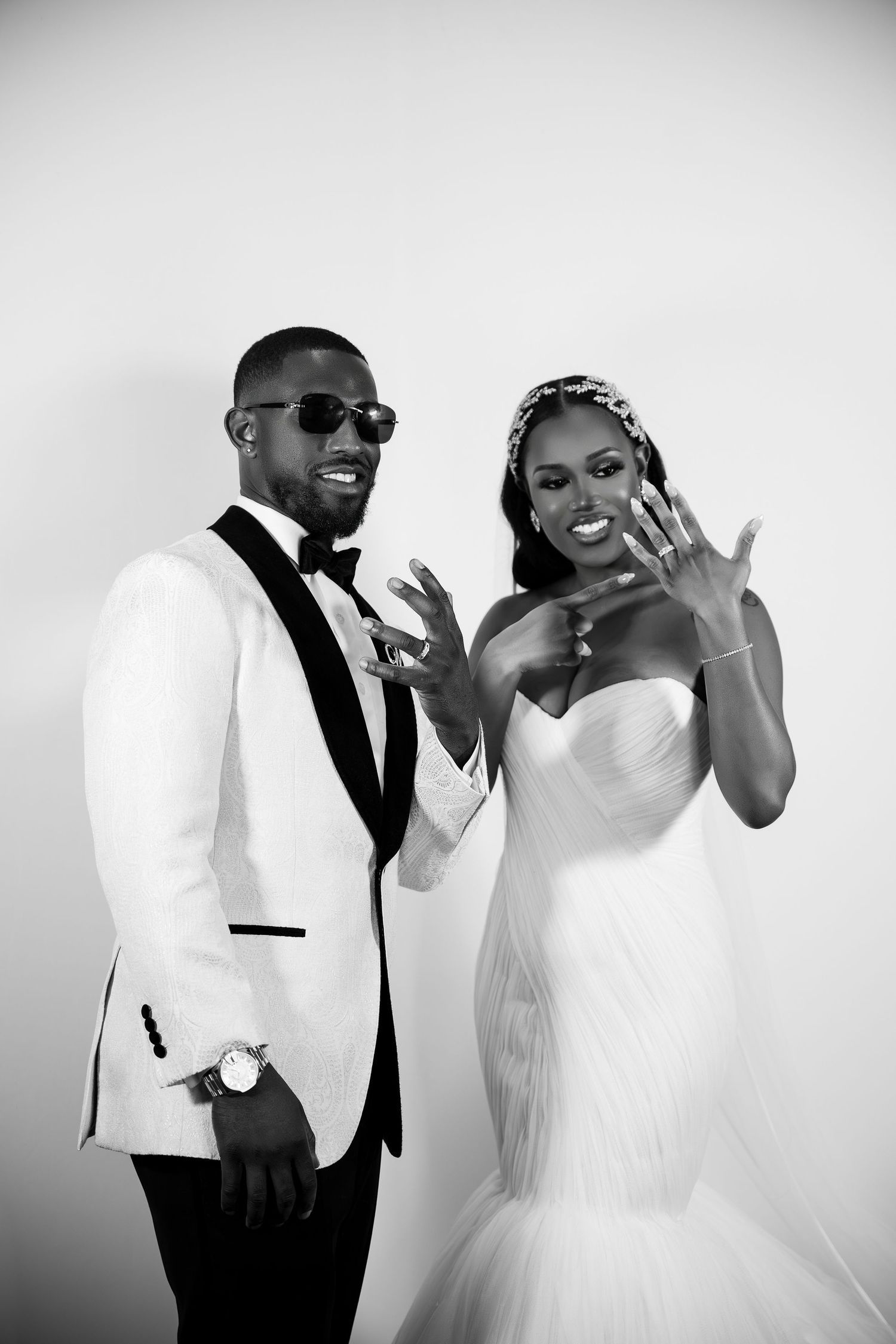 Black and white photo of a joyful newlywed couple in formal attire showing off their rings.