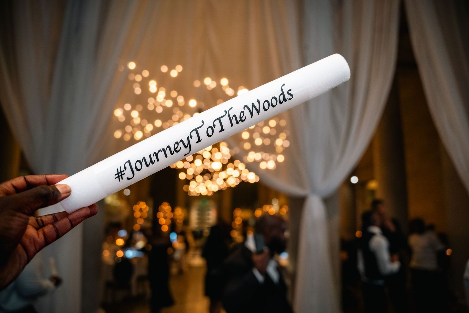 A glowing LED foam stick with #JourneyToTheWoods text at a wedding reception.