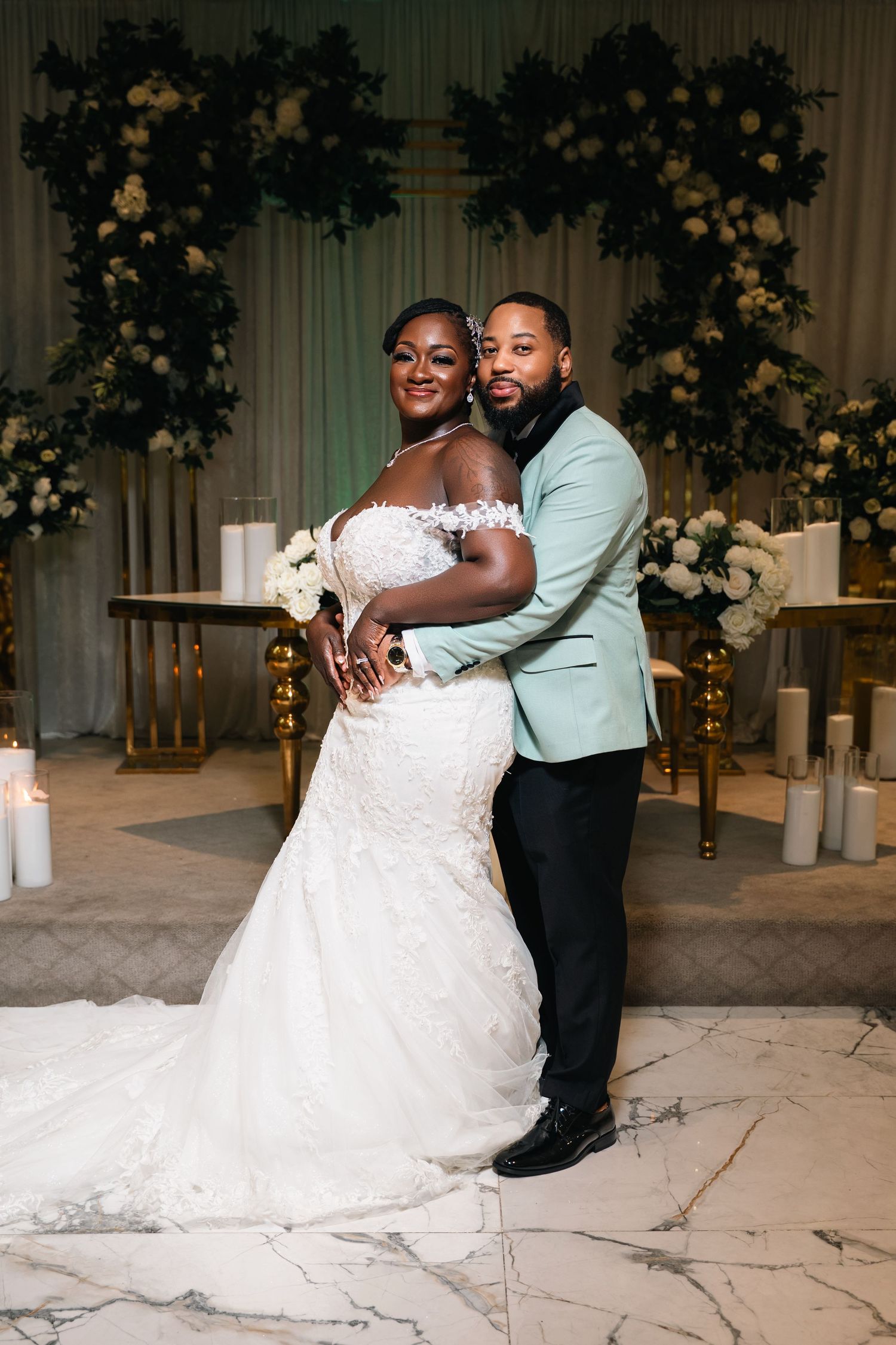 A couple embraces at their wedding ceremony with floral decor and candles in an elegant venue setting.