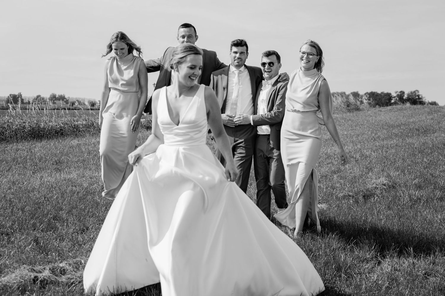 Wedding party walking together across a grassy field in black and white photography.