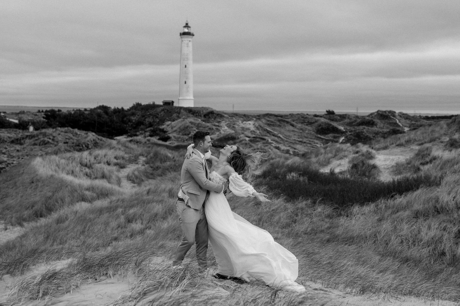 Iconic lighthouse stands tall on grassy coastal dunes under moody grey skies.