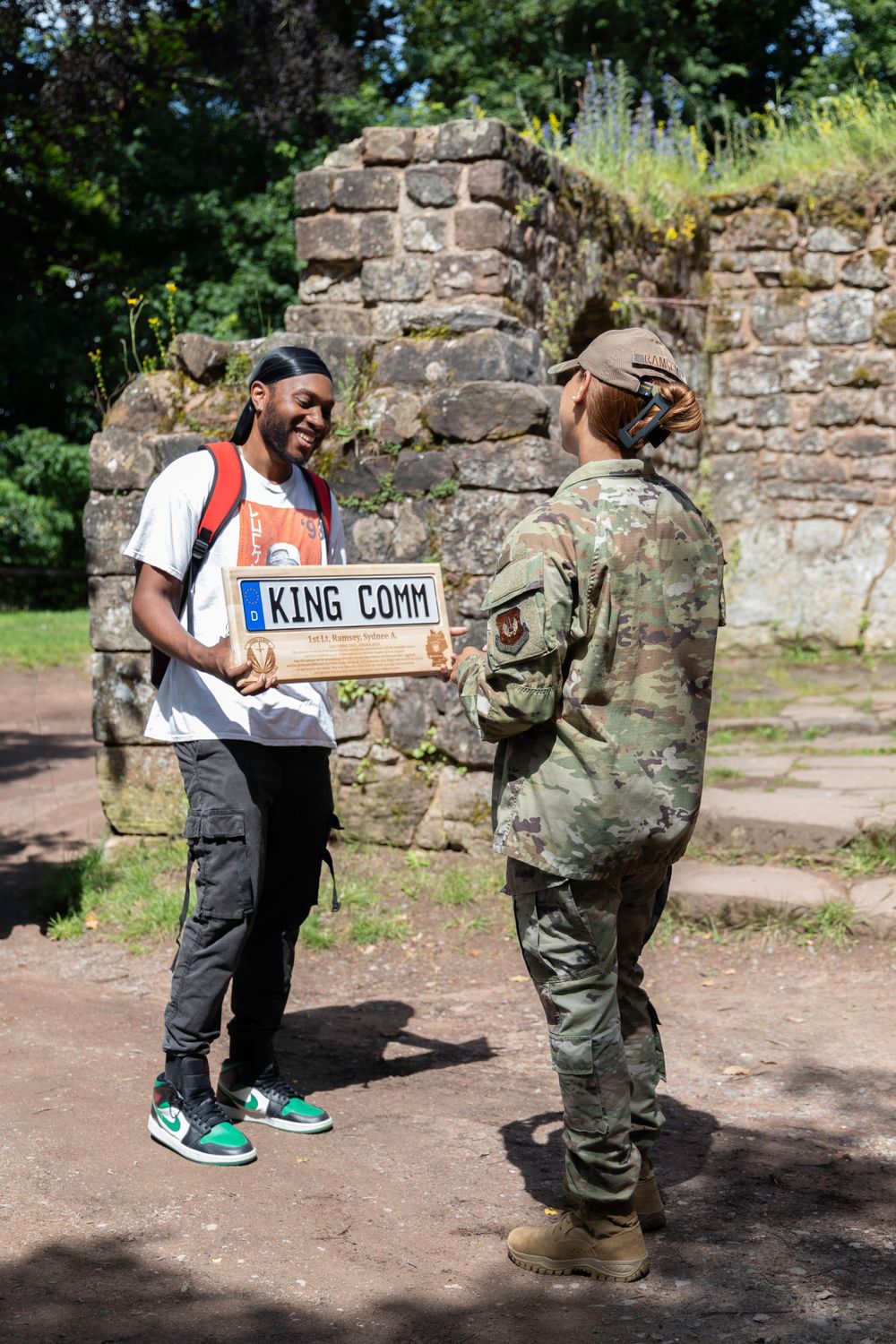 A person in a Home Depot apron chats with someone in military uniform while holding a delivery box outdoors.