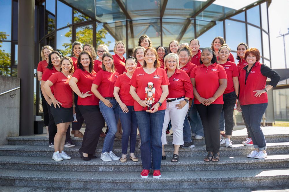 A large group in red shirts stands on outdoor steps for a team photo.