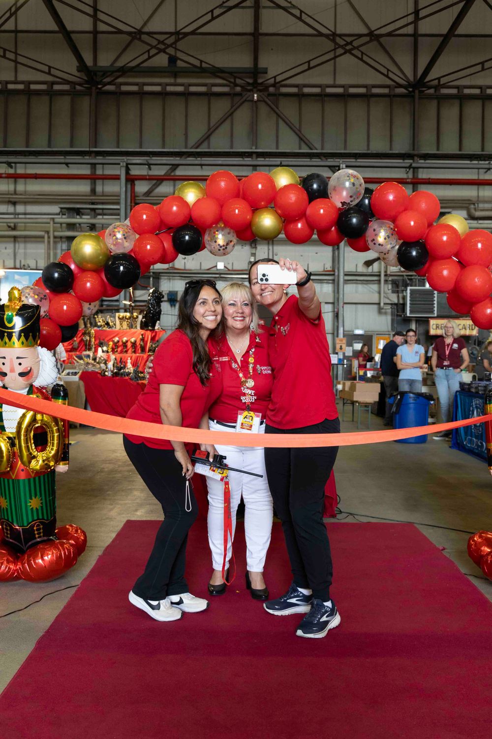 Red and black balloon arch decorates an indoor event with red carpet and autumn decorations.