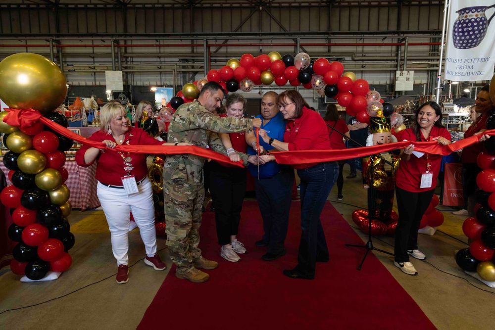 A red ribbon cutting ceremony with balloon arch decorations takes place during a festive event at an indoor venue.