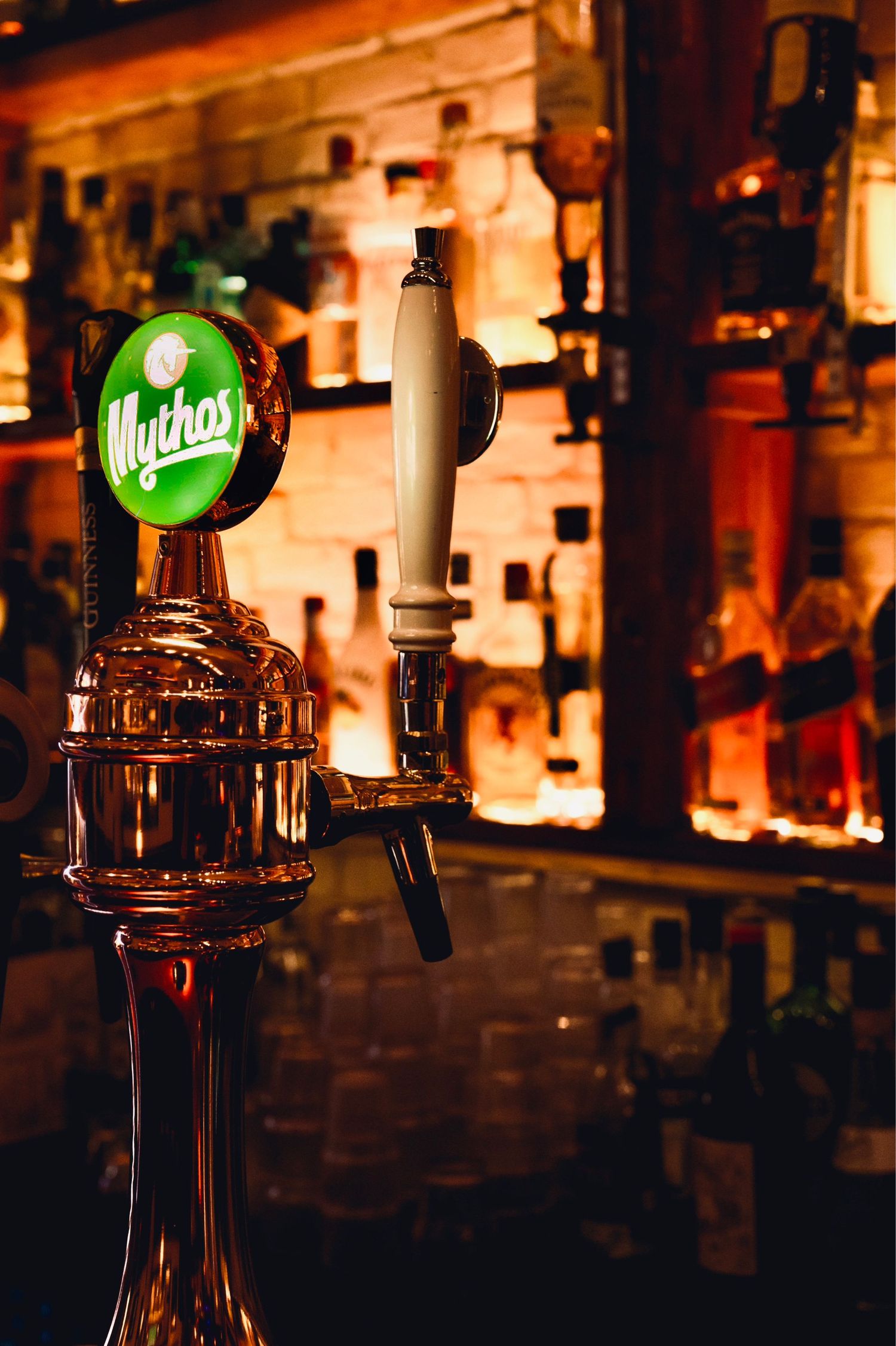Close-up of a vintage beer tap with glowing green Mythos logo at a bar.