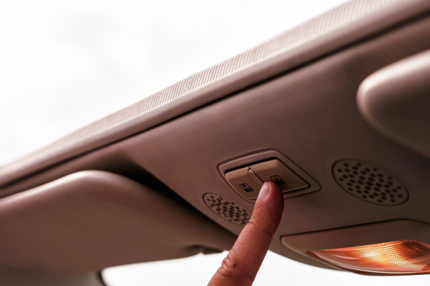 Finger pressing car ceiling control button in beige interior.