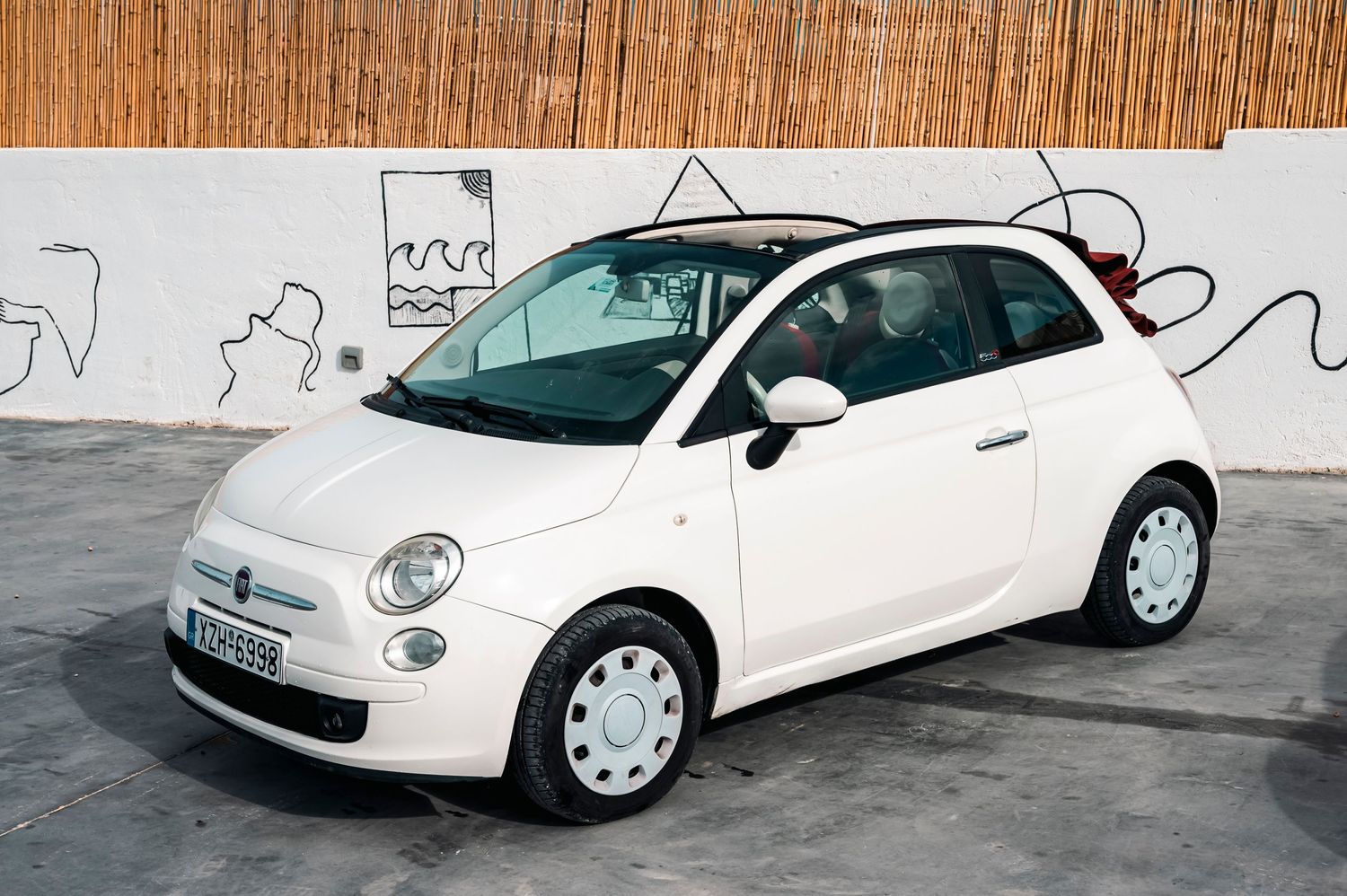 White Fiat 500 parked against a wall with graffiti artwork.