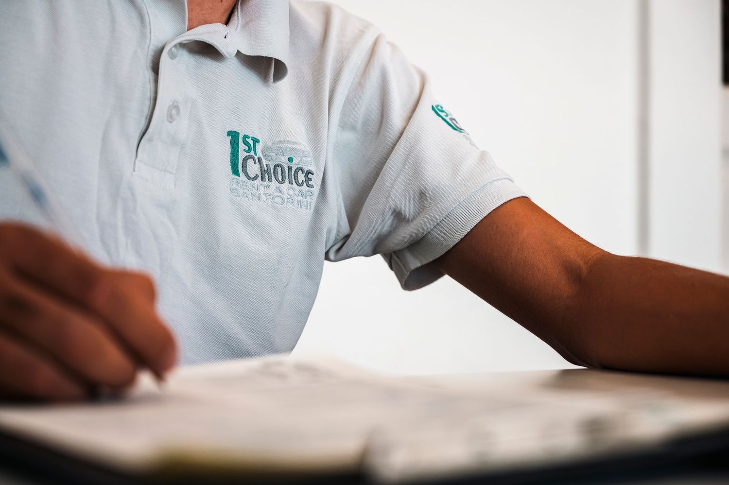Close-up shot of staff member in white uniform with teal logo writing at desk.