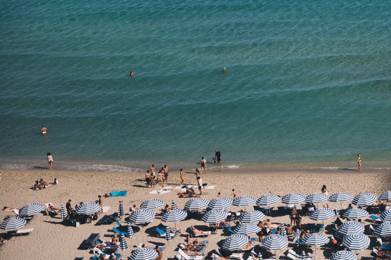 Aerial view of crowded beach with umbrellas and beachgoers dotting the sandy shoreline.