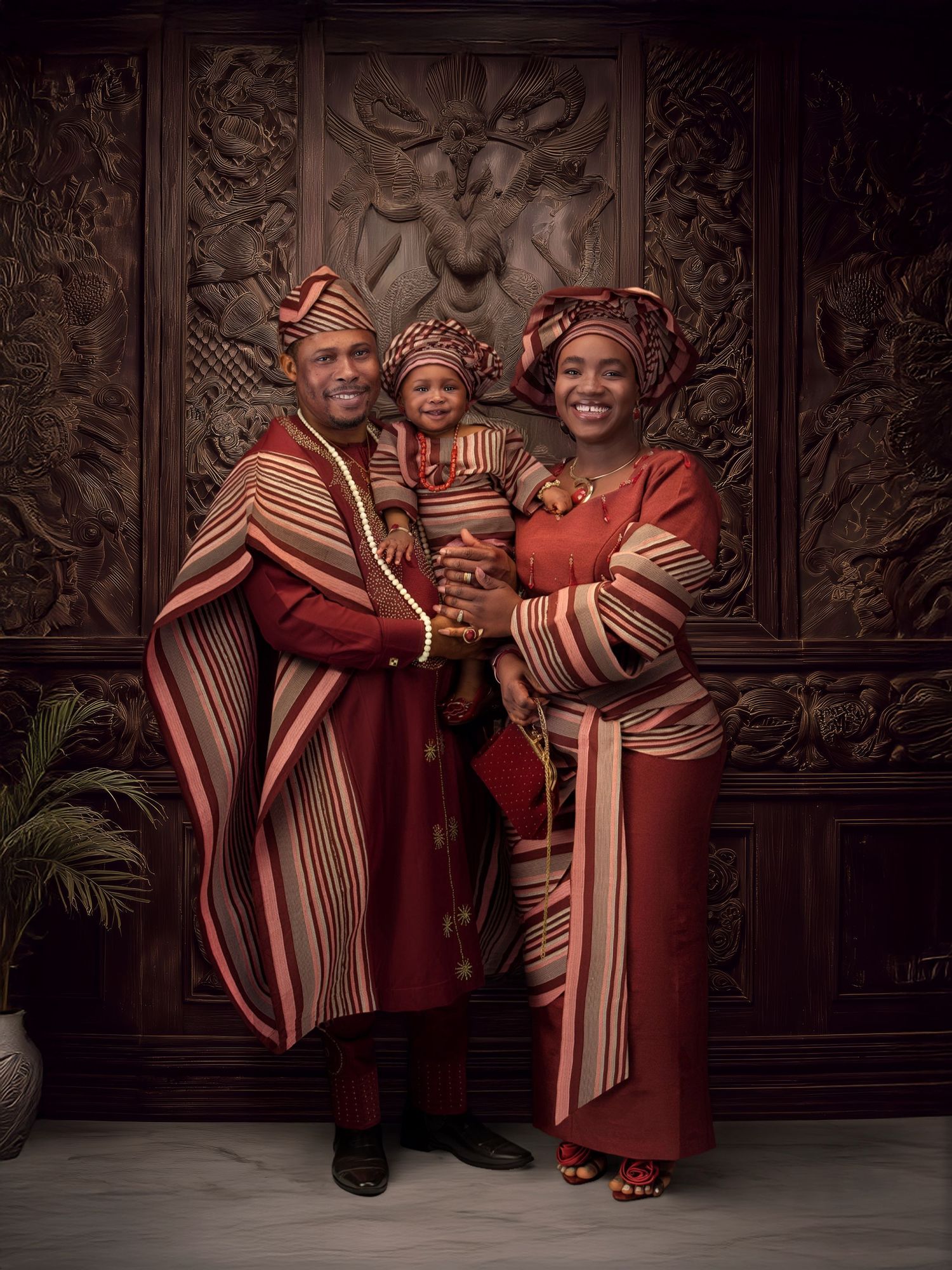 An elegant portrait in warm tones featuring traditional African attire with a red dress and coordinating pink and striped headwrap.