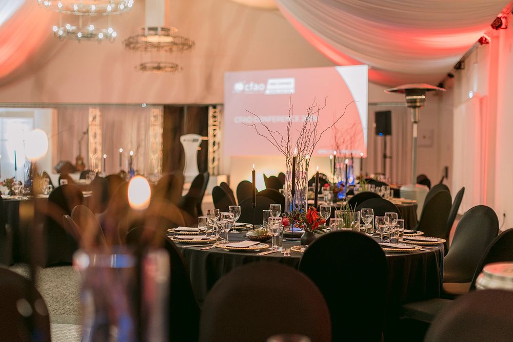 Elegantly decorated corporate gala dinner venue with black round tables, candelabras, and a projection screen on stage.