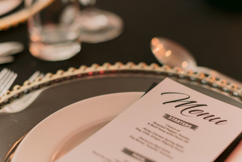 Elegant wedding menu card on a pink plate with gold-beaded charger at a formal dinner table setting.