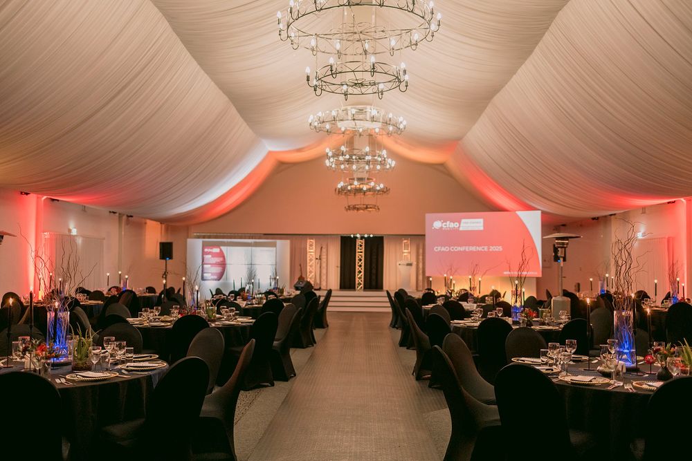 Elegant event venue with chandelier lighting, round tables, black chairs, and red ambient uplighting.