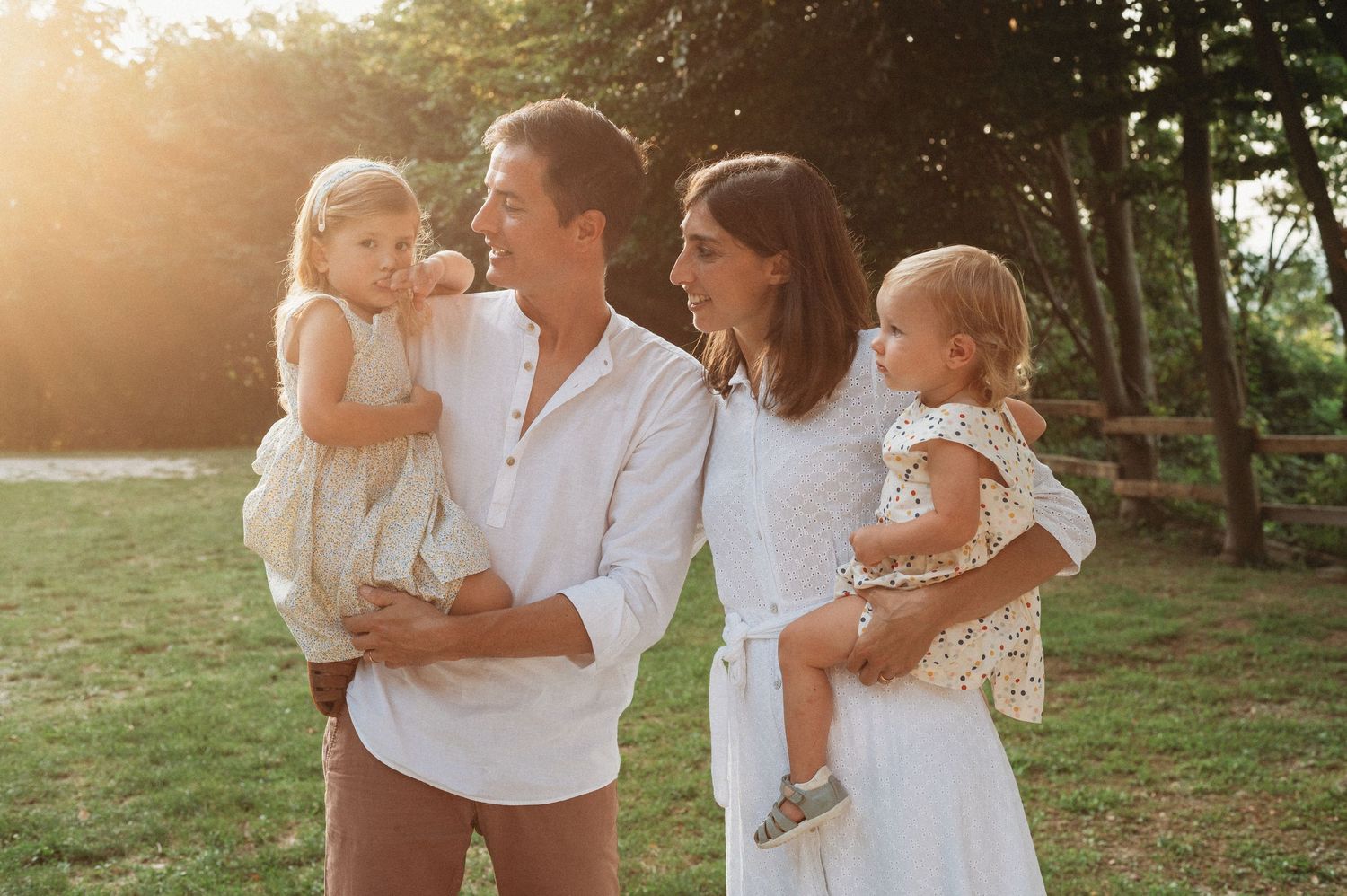 Four people wearing white outfits embrace outdoors during golden hour in a natural setting.