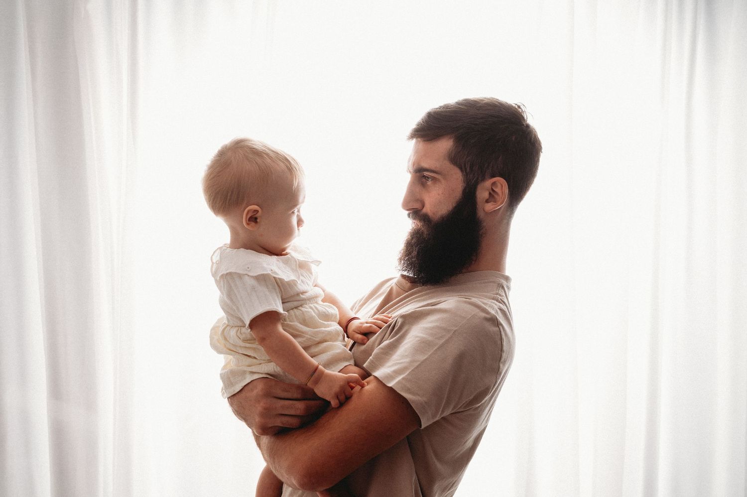 Two silhouettes of parent and baby against a bright window create a tender bonding moment at home.