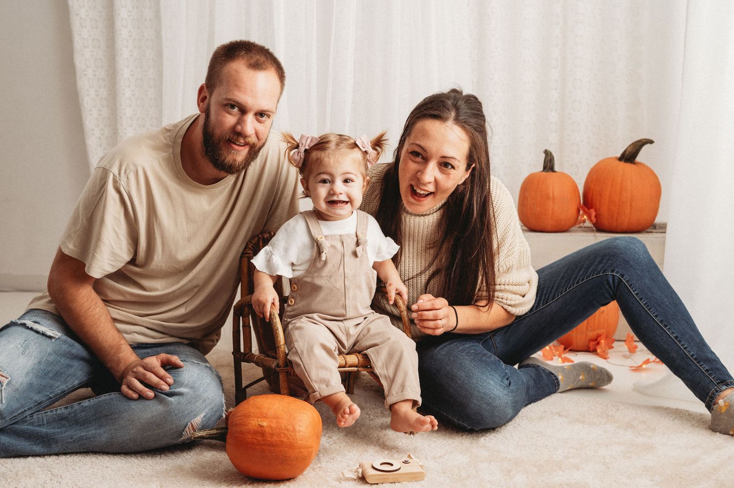 Family sits together on floor with pumpkin decorations in a warm, cozy home setting during autumn season.