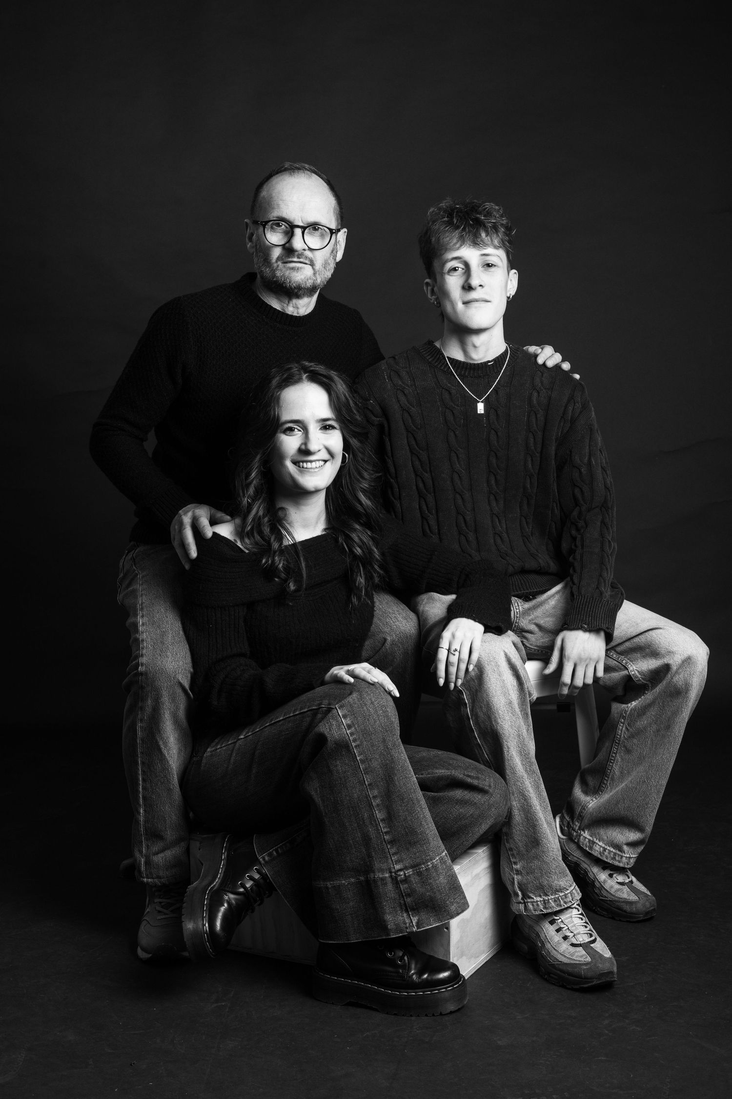 Black and white portrait series showing casual posed studio shots of people sitting together against dark background.