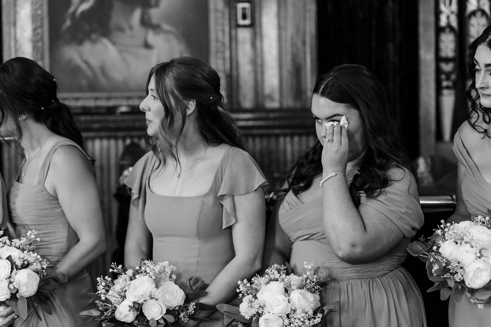 Bridesmaids holding white bouquets pose together in a row while wearing matching gray strapless gowns.