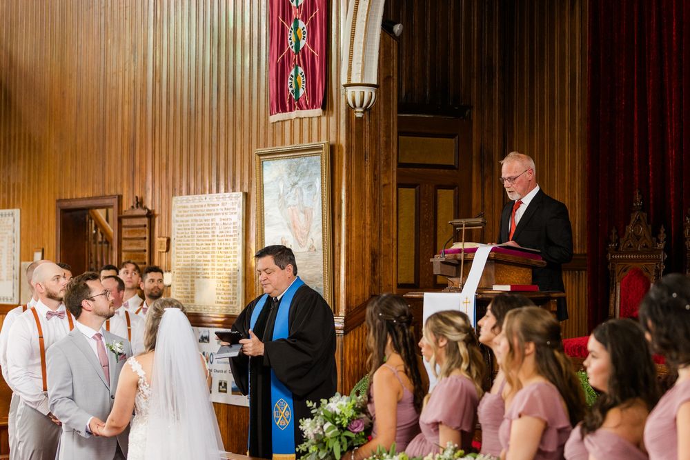 A traditional church wedding ceremony shows the bridal party standing at the altar surrounded by wood paneled walls and decor.