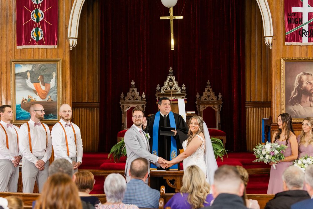 Beautiful church wedding ceremony with pink and purple floral arrangements lining the elegant wooden pews.