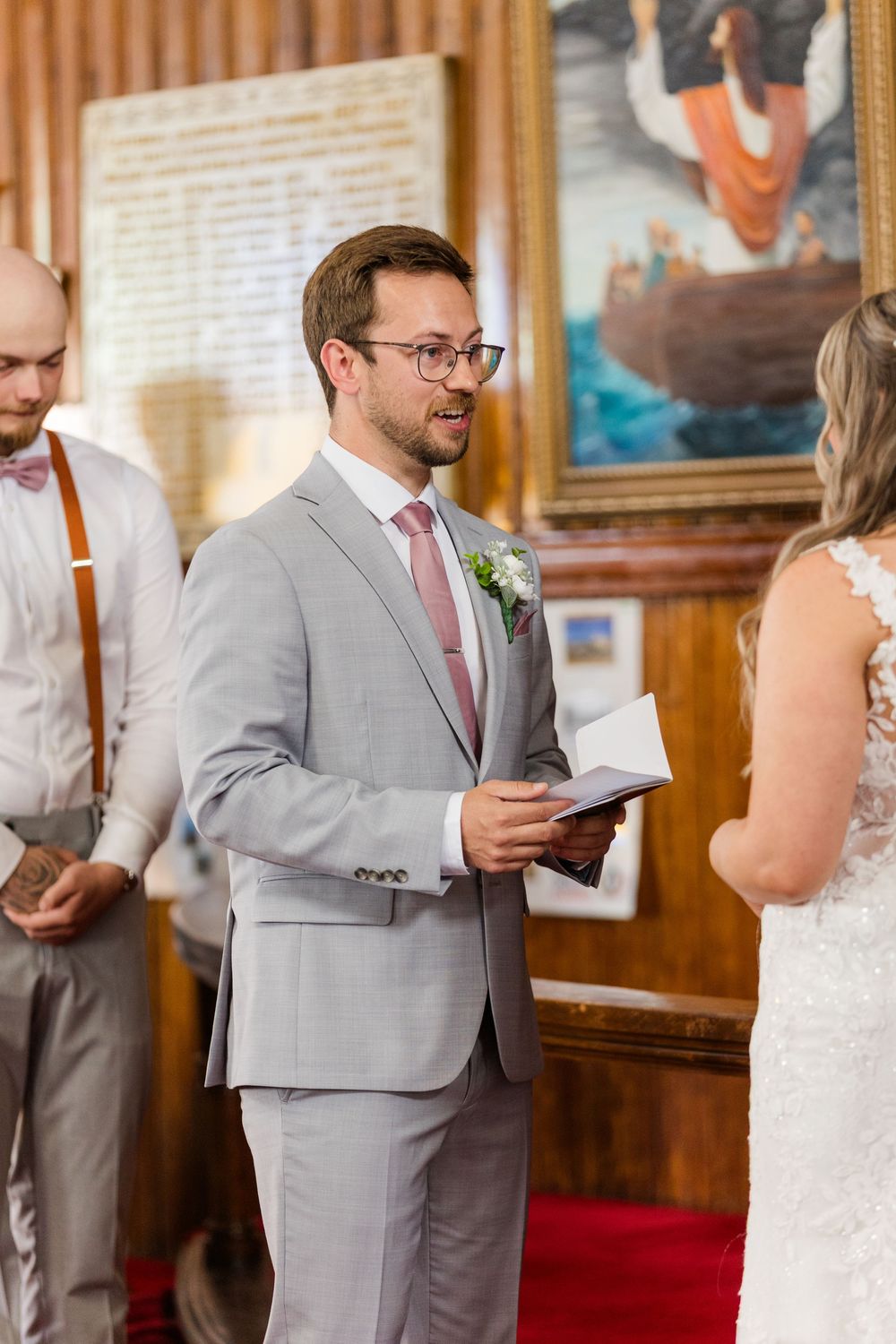 Members of a wedding party in gray suits stand in line reviewing papers during a ceremony.