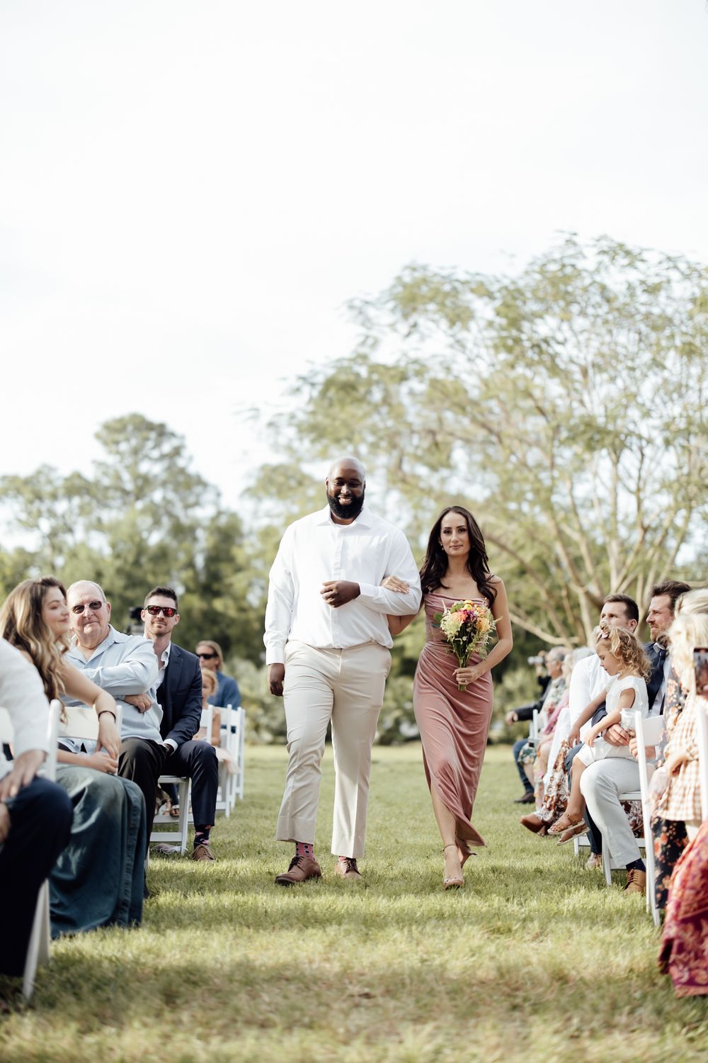 Wedding guests jump and dance together on a grassy outdoor celebration field.