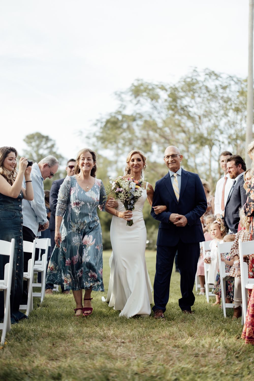 Wedding guests mingle during an outdoor ceremony with white chairs on a grassy lawn.