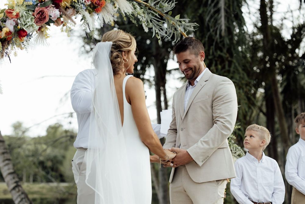 A happy couple celebrates their wedding day with an outdoor ceremony surrounded by beautiful floral arrangements and trees.