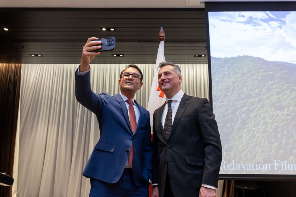 Delegates taking a selfie at a diplomatic reception with flag backdrop.