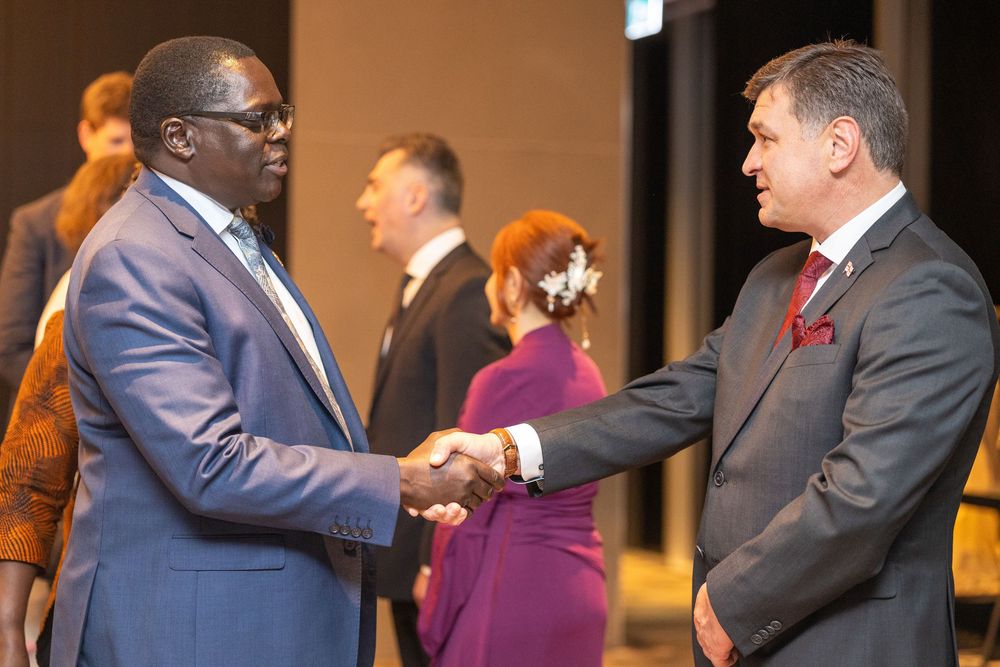 Dignitaries shaking hands during an embassy reception, protocol backdrop.