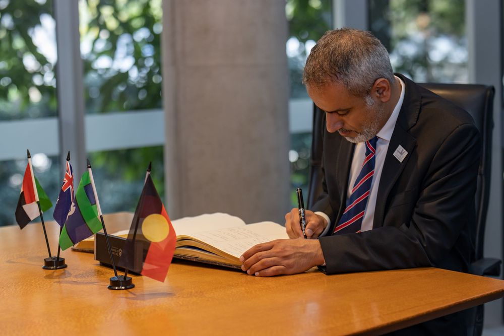 Signing ceremony with officials at a table, Australian and partner nation flags behind.