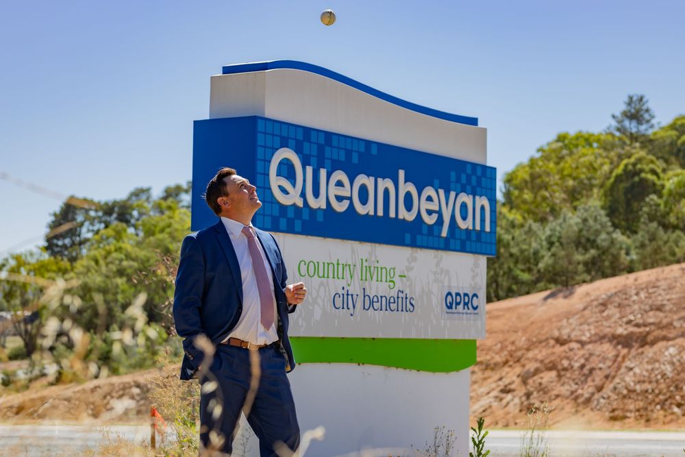 Queanbeyan welcome sign with official standing beside the roadside landmark on the ACT–NSW border.